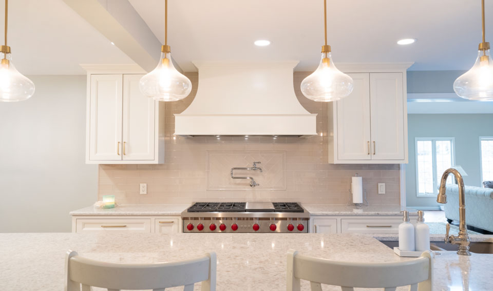 An after photos of a kitchen remodel. white oven hood sits a top a stove. The cabinets and countertop are also white.