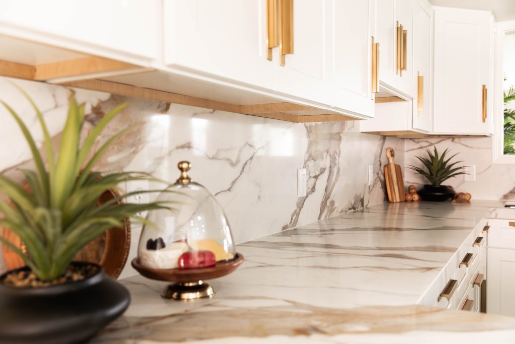 Closeup of a renovated kitchen with white marble countertops and white cabinets. 