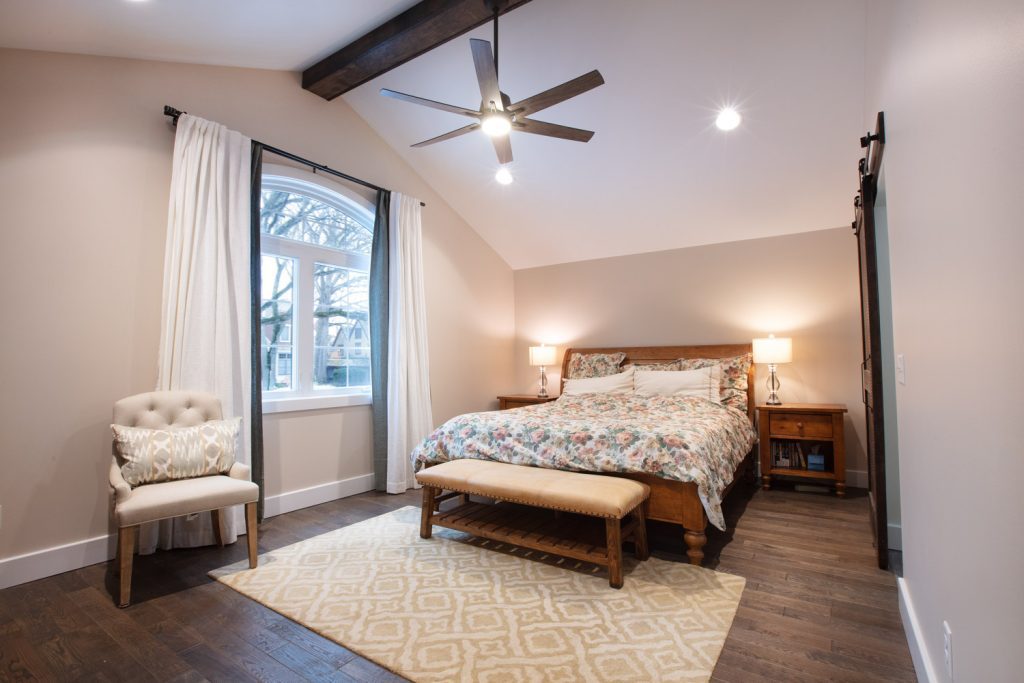 Recently renovated master bedroom with painted walls, a dark wood beam on the ceiling and a modern fan. 