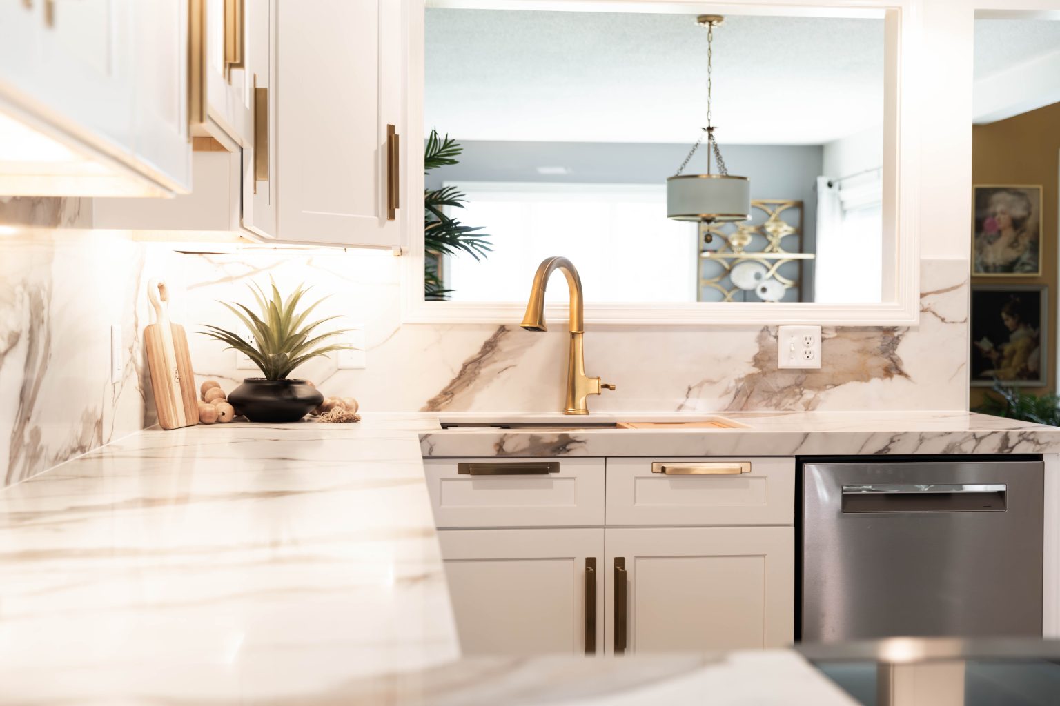 Closeup of a under cabinet lighting with white countertops, white cabinets and a gold faucet and hardware.