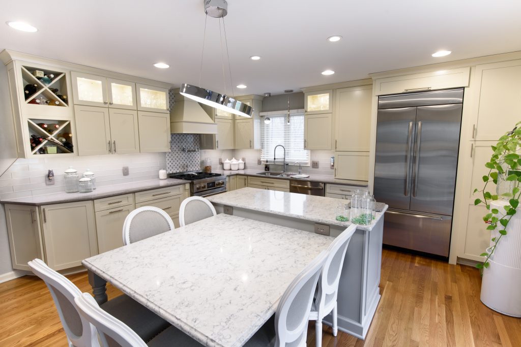 Bright modern kitchen with white cabinets, marble countertops, and a stainless steel double-door refrigerator.